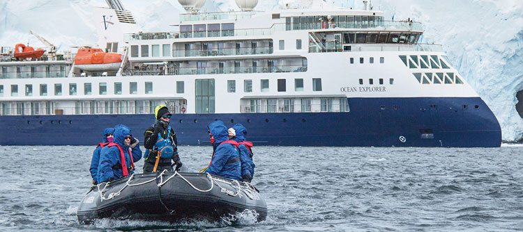 Zodiac boat with passengers moving to shore with Ocean Explorer in the background, Antarctica